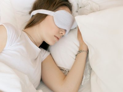 A serene scene of a woman sleeping with a white sleep mask in a cozy bed.